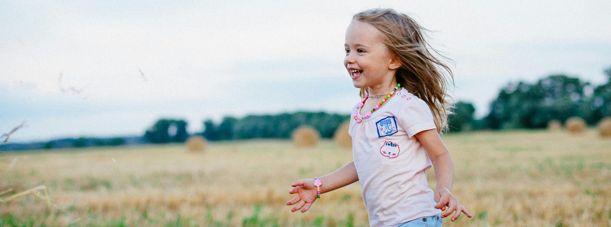 A girl smiling and walking in a field of wheat, sunny day