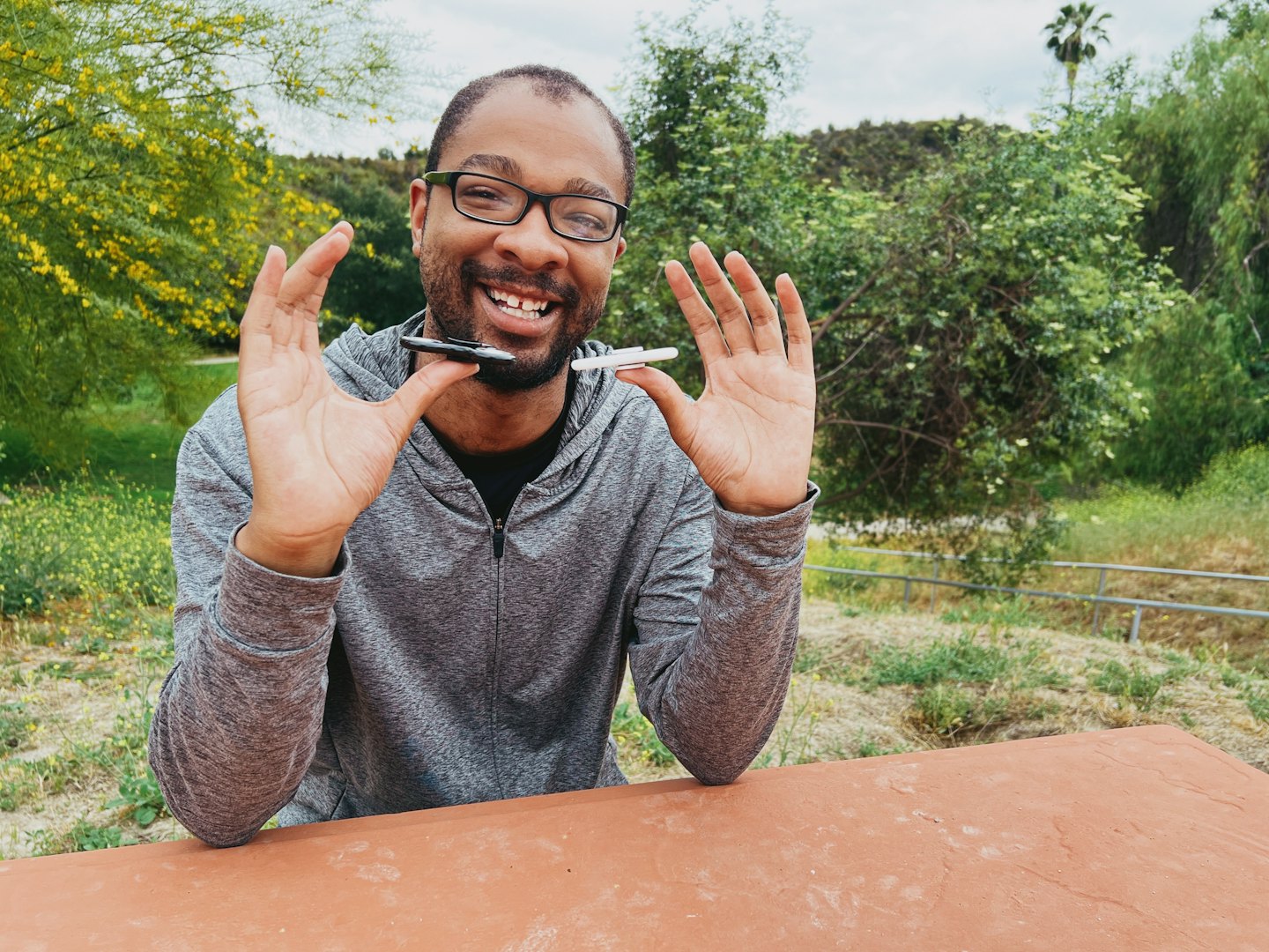 Smiling person sitting outdoors in a sunny day, balancing a pen on his figures